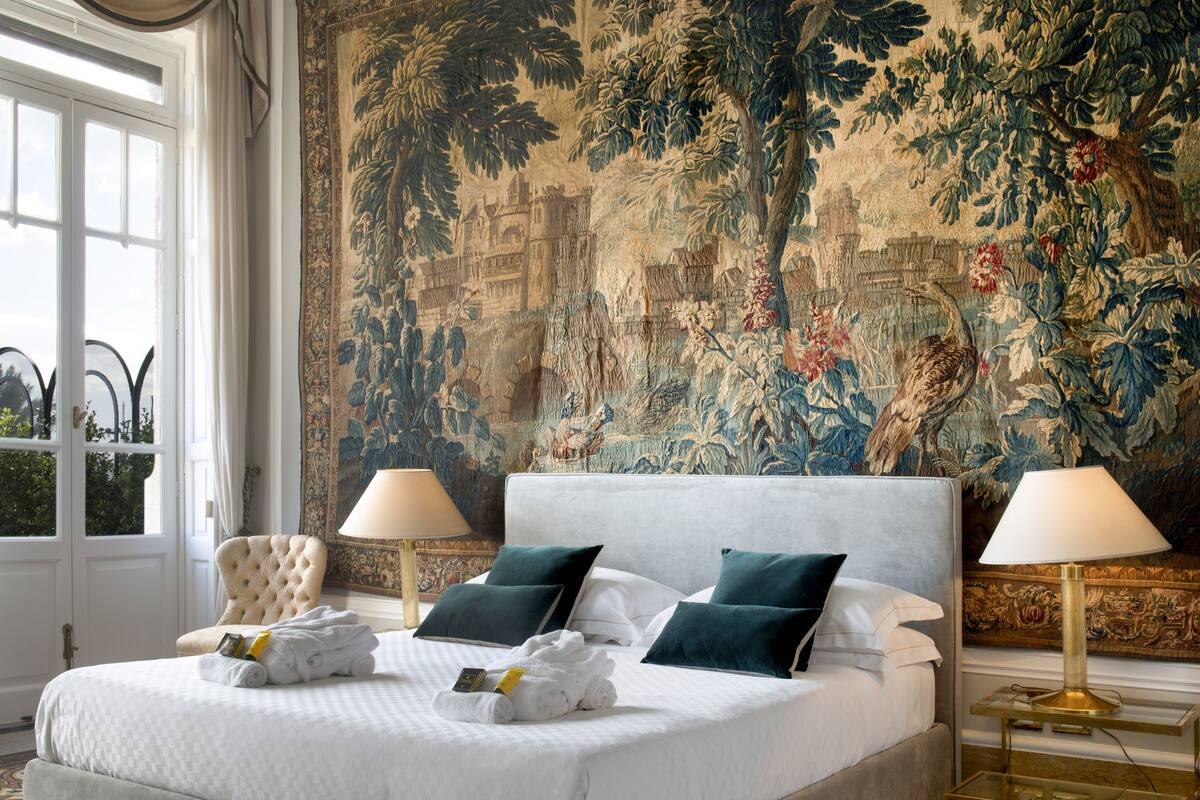 Une chambre spacieuse avec un grand lit, deux tables de chevet et une tapisserie richement décorée au mur.