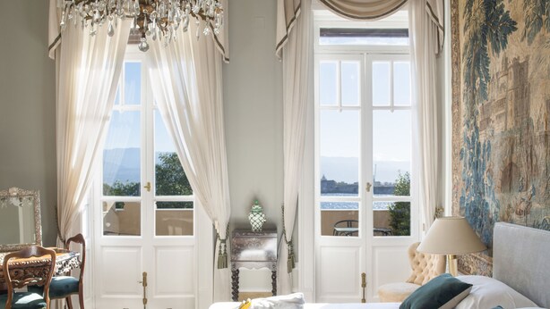 A hotel room with a bed, two chairs, a table, a chandelier, and a view of the outdoors. - Vittoria - house of charme (Messina)