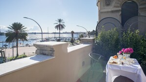 A terrace with a table set for breakfast overlooking a marina with boats and palm trees. - Vittoria - house of charme (Messina)
