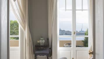 Une chambre d’hôtel avec un grand lit, un lustre, une vue sur la mer et un balcon avec une chaise.