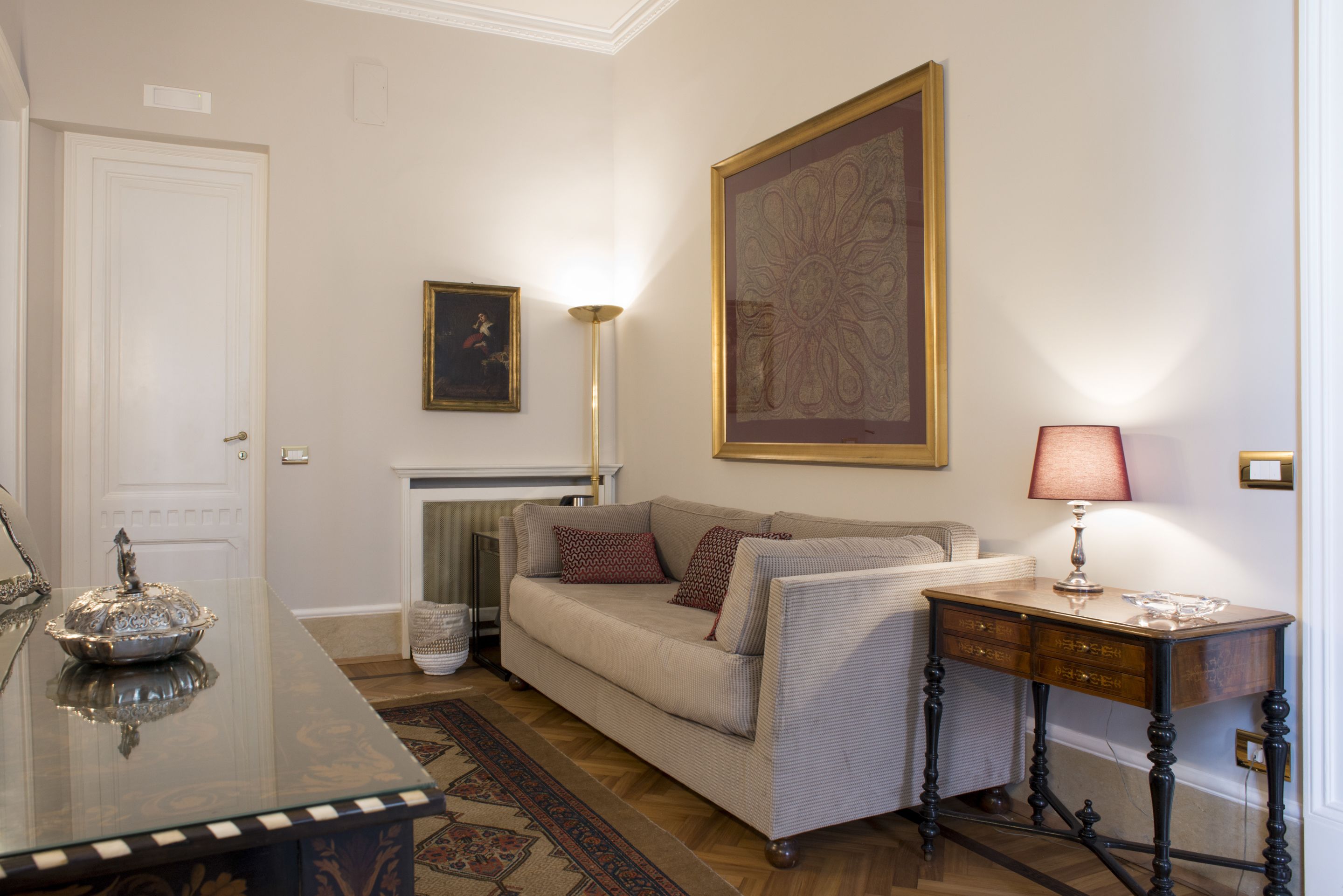 Una sala de estar con un sofá, una mesa con lámpara, una chimenea y un cuadro grande en la pared.