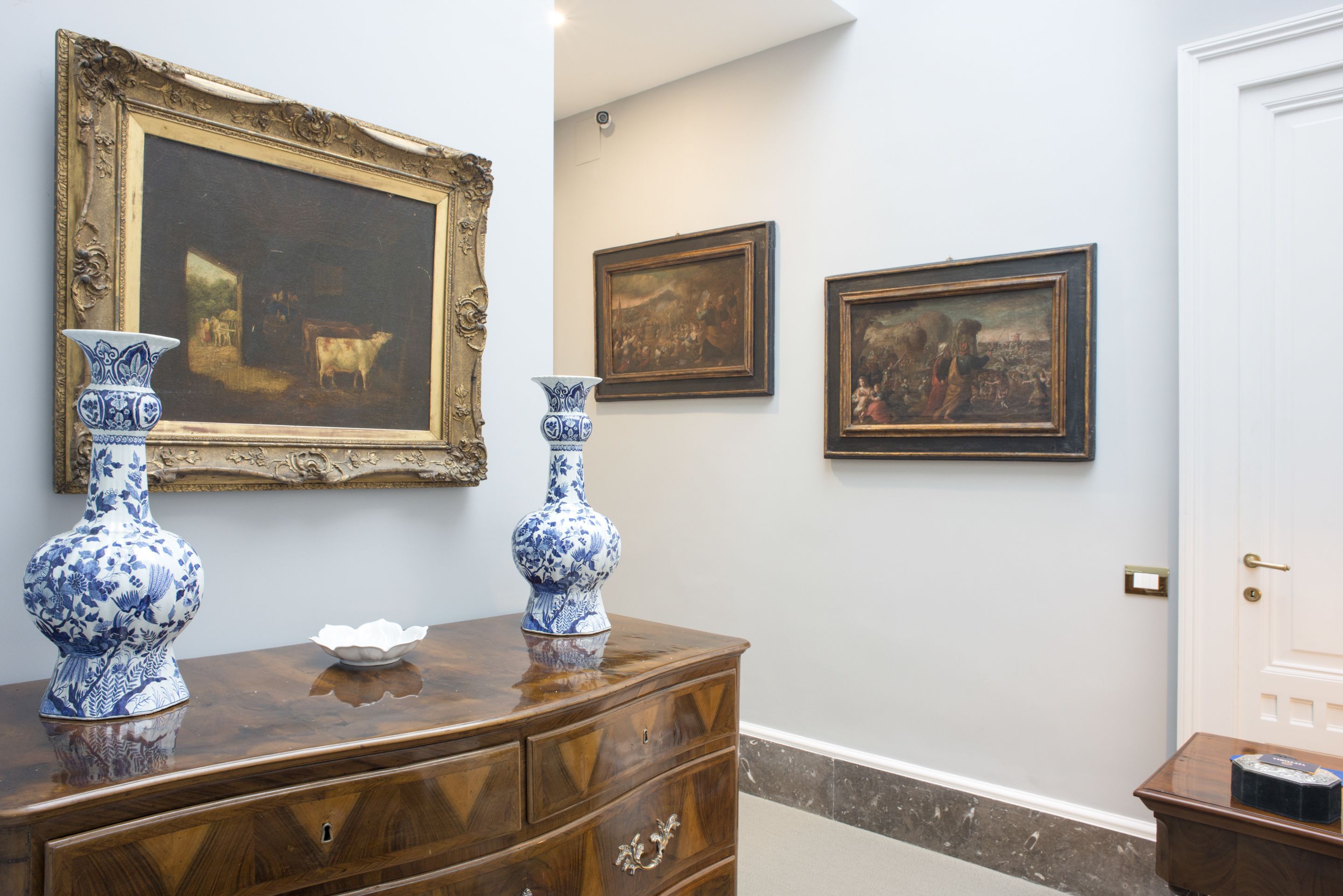 A hallway with a wooden dresser, two vases, and three framed paintings on the wall.