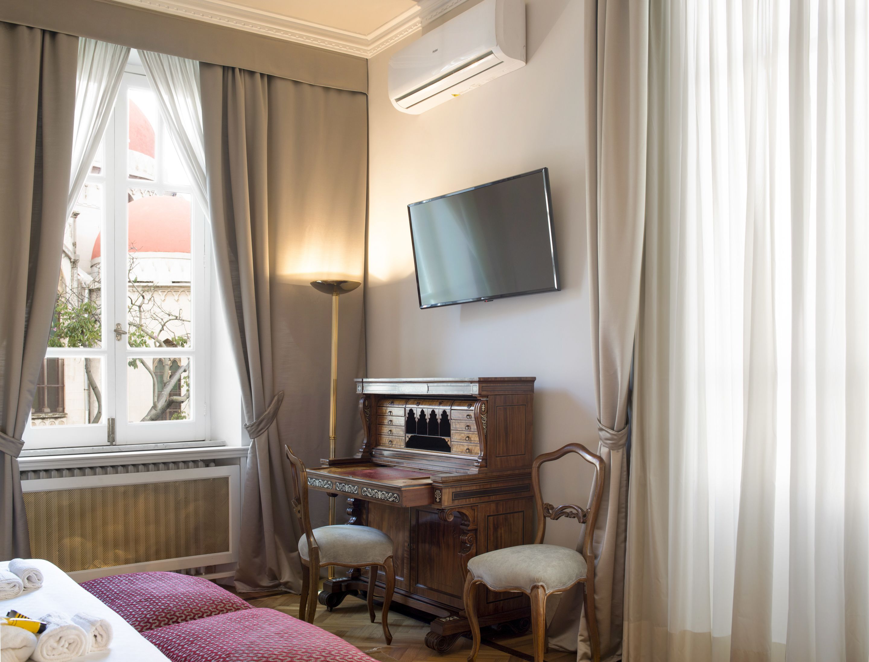 Une chambre d’hôtel comprenant un lit, deux chaises, un bureau avec des tiroirs, un téléviseur à écran plat et une fenêtre avec des rideaux.