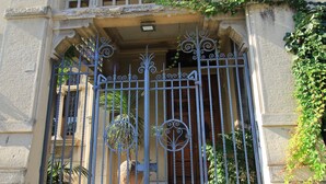 A building with a large, ornate metal gate, a stone facade, and a balcony with plants. - Vittoria - house of charme (Messina)
