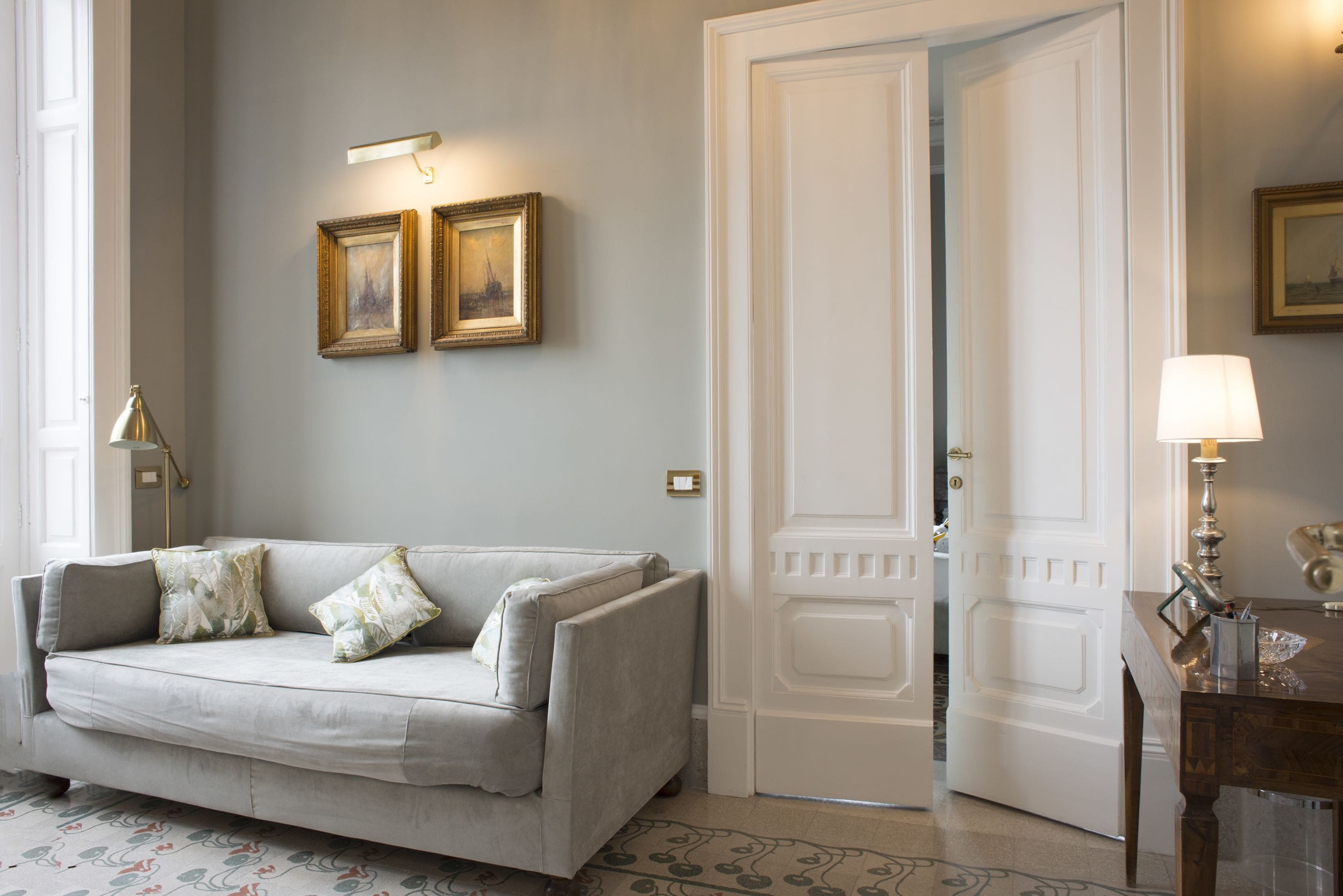 Ein Zimmer mit einem hellen Sofa, einer Tür, einer Lampe und gerahmten Bildern an der Wand.