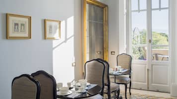 Un coin repas avec une table dressée pour quatre personnes, deux œuvres d’art encadrées accrochées au mur et une grande fenêtre donnant sur un paysage verdoyant.