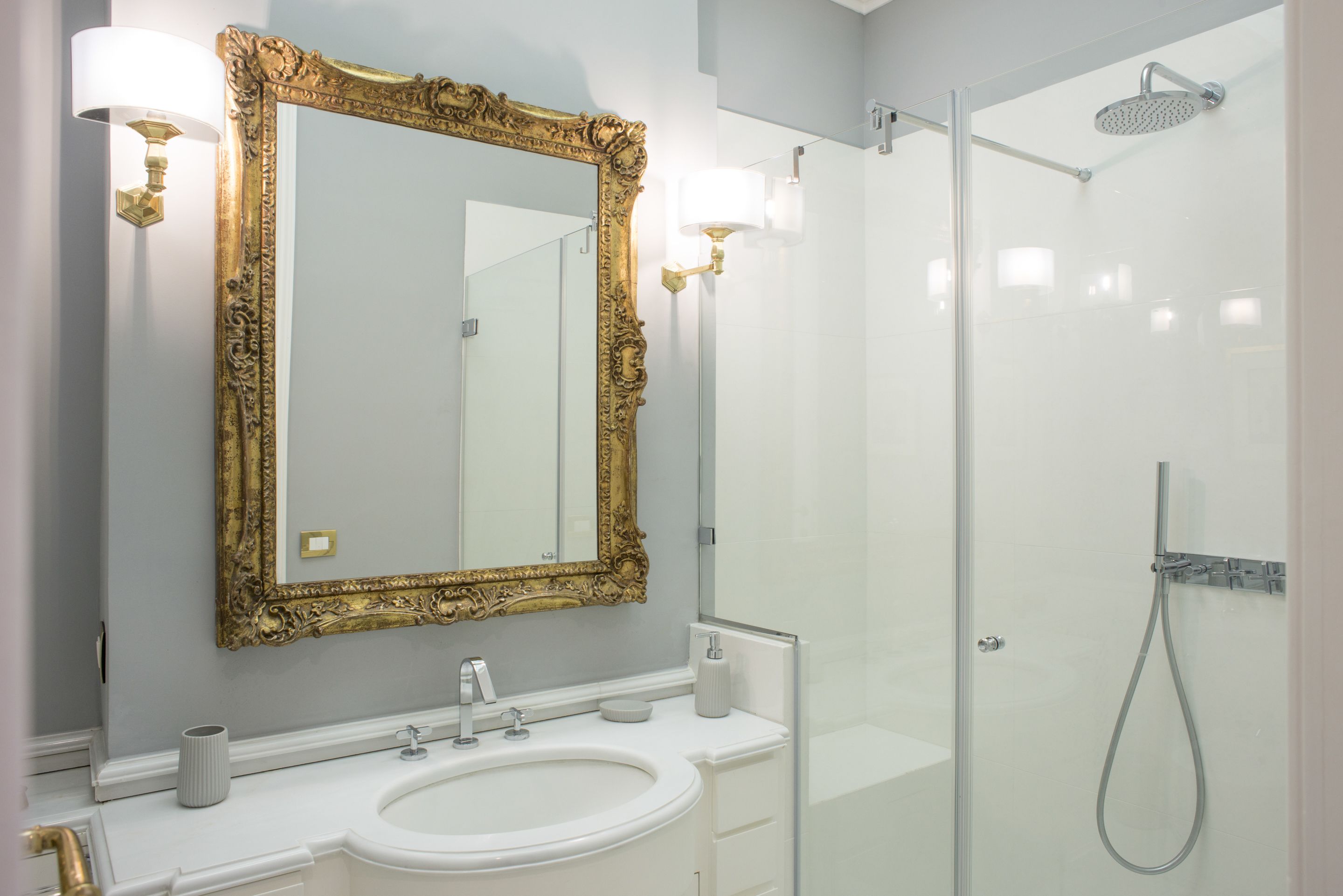 A bathroom with a large ornate mirror, a sink, and a glass-enclosed shower.