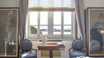Ein Hotelzimmer mit großem Fenster, zwei Stühlen, einem kleinen Tisch mit einer Vase und Bildern an den Wänden.