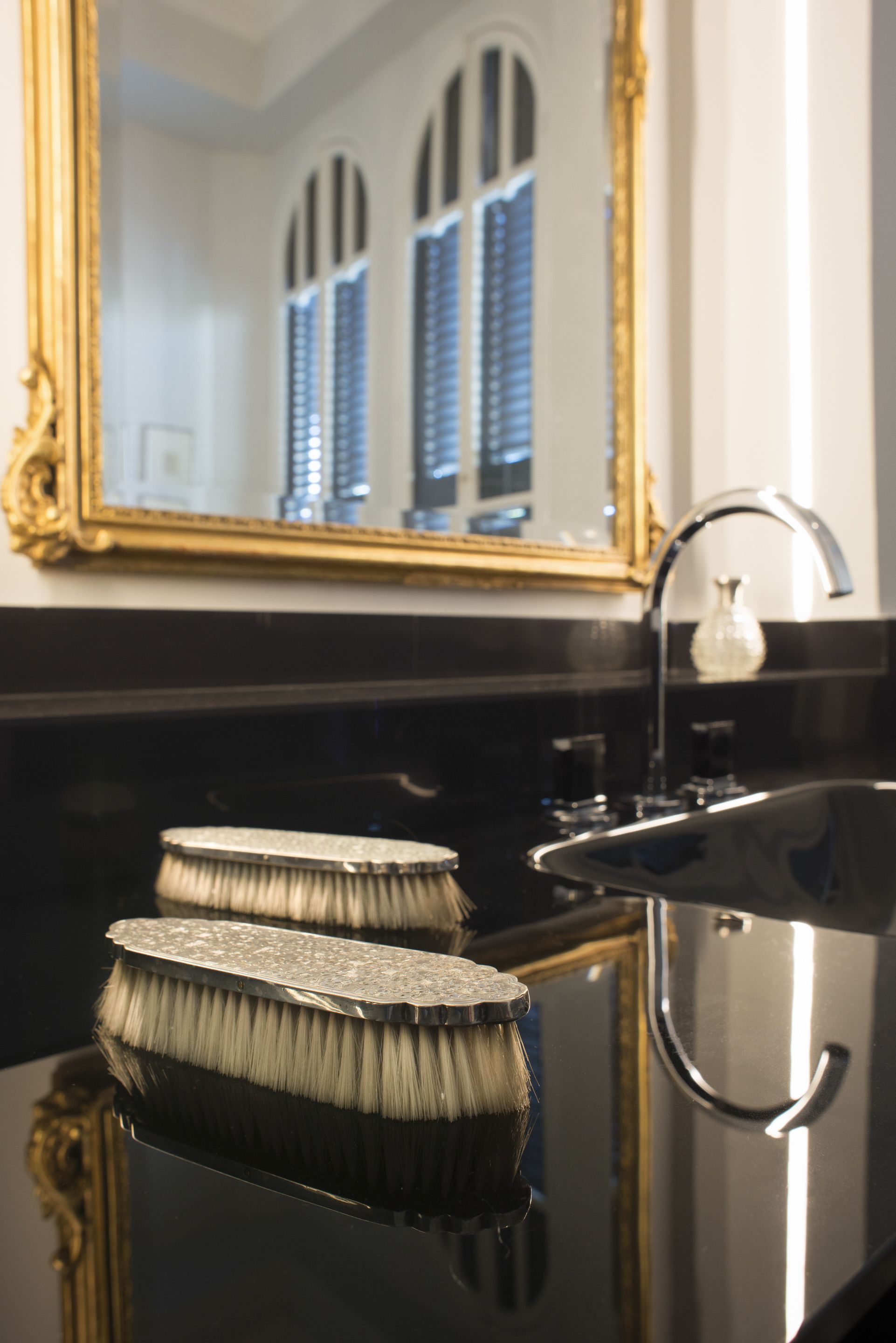 A bathroom with a black sink, a gold-framed mirror, and a window with blue shutters.