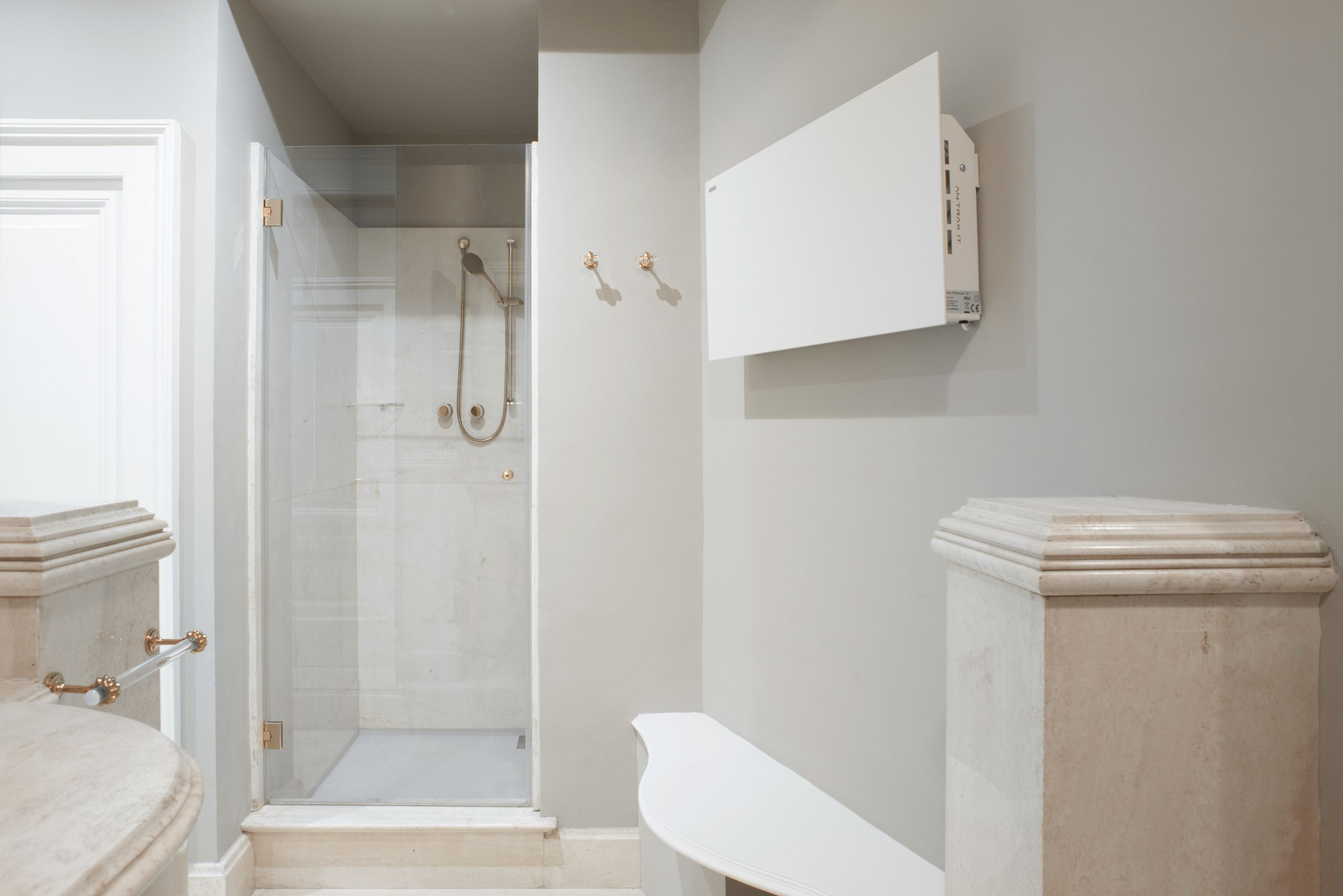 A bathroom with a glass-enclosed shower, a white vanity, and a marble pedestal sink.