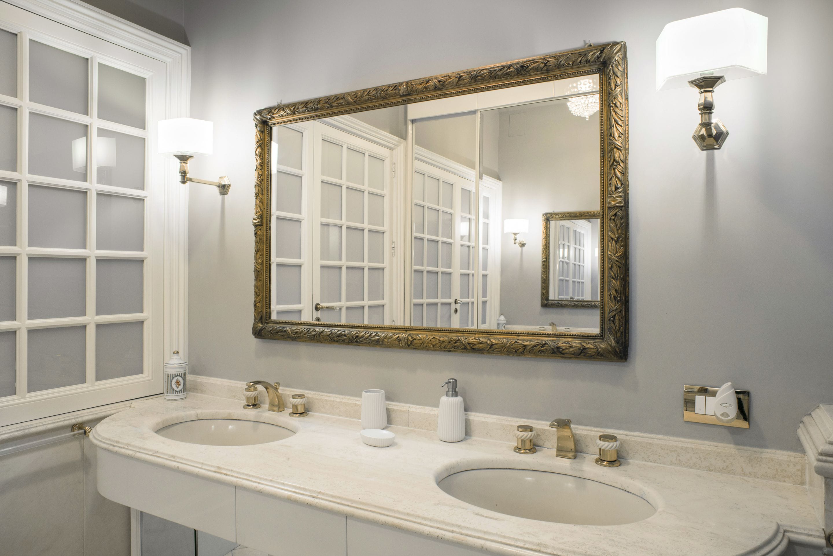 A bathroom with two sinks, a large mirror with an ornate frame, and wall-mounted lights.