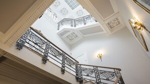 A grand staircase with ornate black railings and a high ceiling with decorative patterns. - Vittoria - house of charme (Messina)