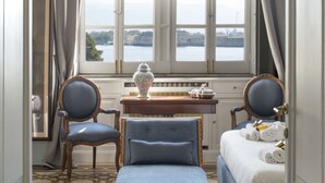 A room with a large window, a chandelier, a desk with a vase, two chairs, a bed with towels, and patterned flooring. - Vittoria - house of charme (Messina)