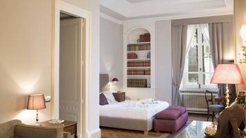 A hotel room with a bed, bedside table, lamp, bookshelf, and a window with curtains.