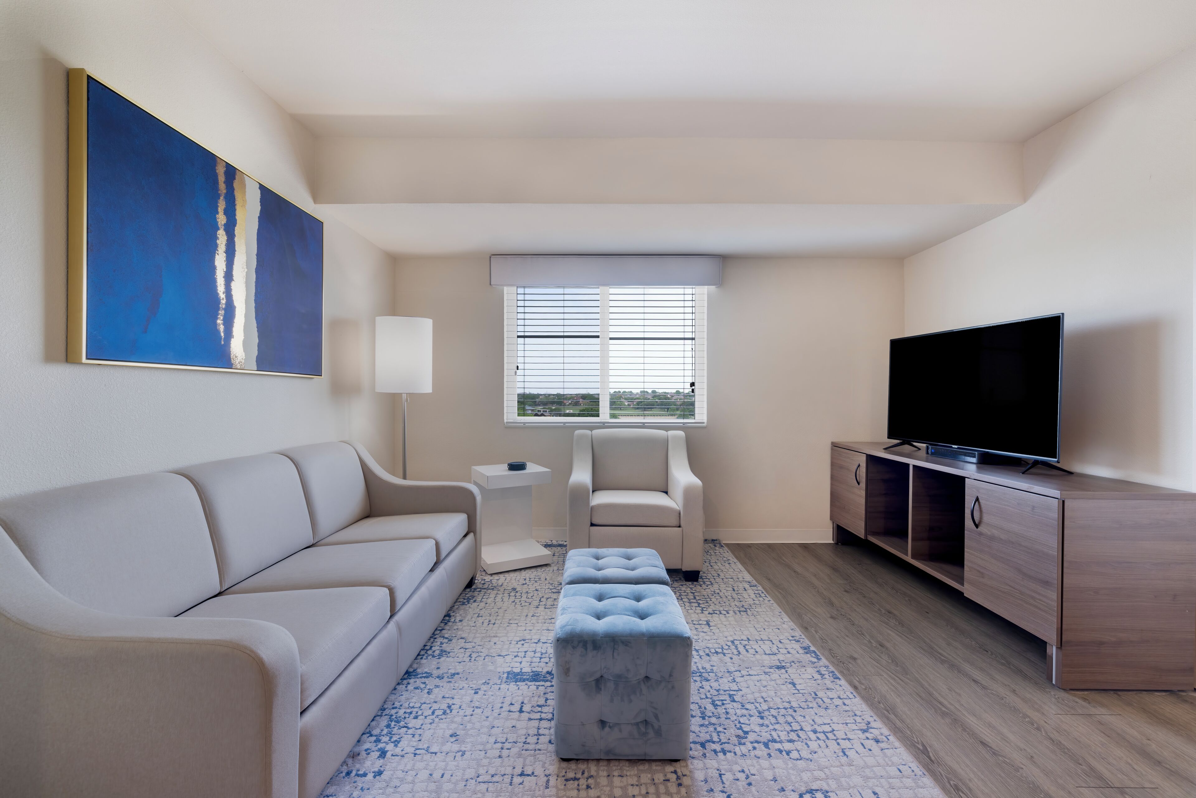 Una sala de estar moderna con sofá, reposapiés, mueble para televisión y una obra de arte en la pared.