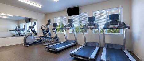 Un gimnasio con cintas de correr, elípticas y un espejo grande.
