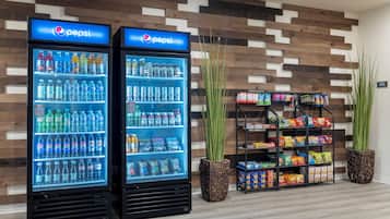 Two Pepsi refrigerators stocked with beverages, a snack display, and tall plants.