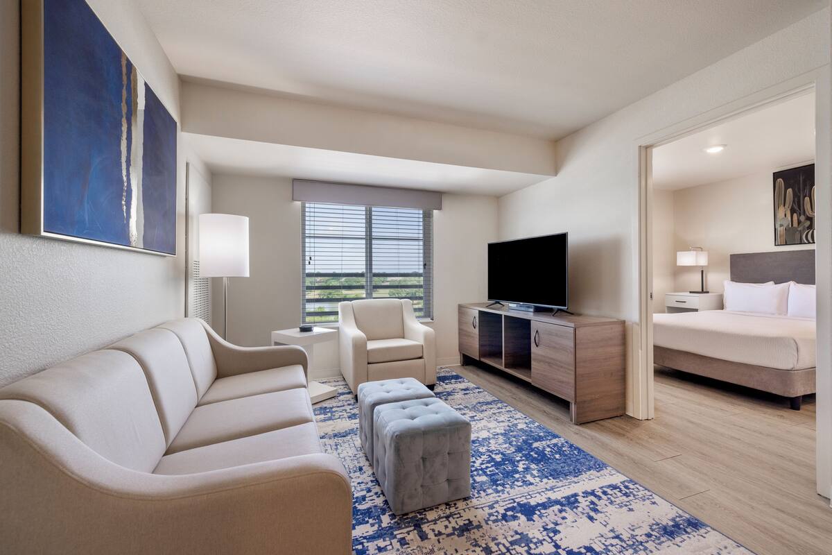 A modern hotel room with a sofa, ottoman, TV, and a bed.