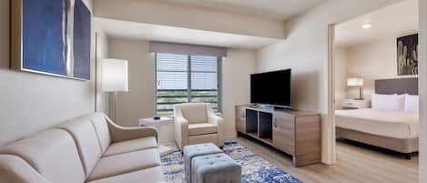 Una habitación de hotel moderna con sofá, reposapiés, televisión y cama.