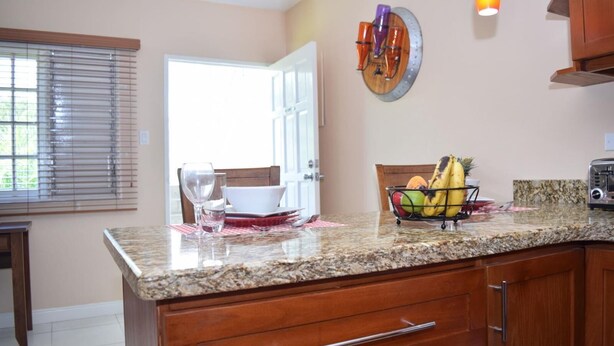 A kitchen with granite countertops, wooden cabinets, and a fruit bowl on the counter. - The Barcelona by Pro Homes Jamaica (Kingston)