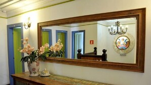 A reception area with a large mirror, a vase of flowers, a chandelier, and a framed artwork on the wall.