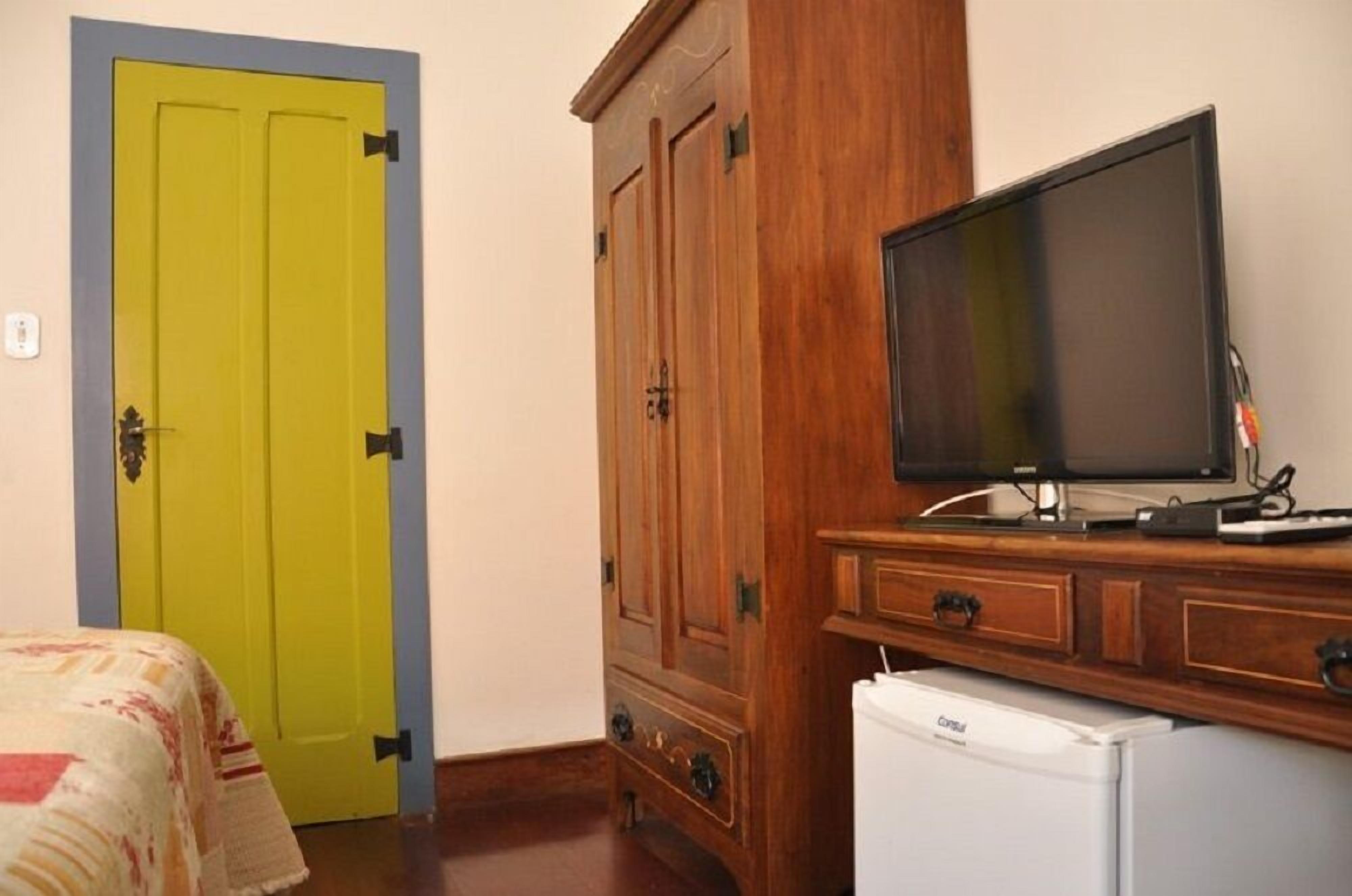 A room with a yellow door, a wooden cabinet with a television, and a white refrigerator.