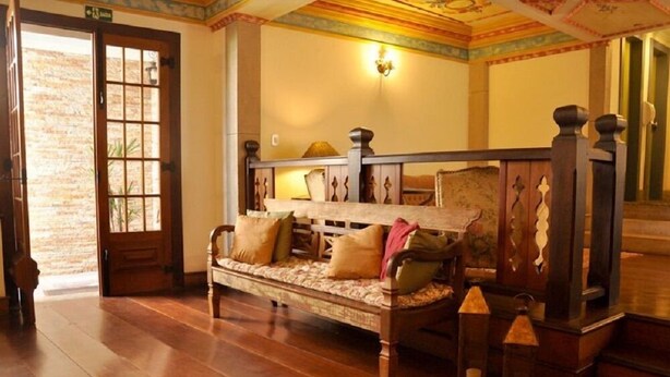 A wooden bench with cushions in a room with wooden flooring and a decorative ceiling.