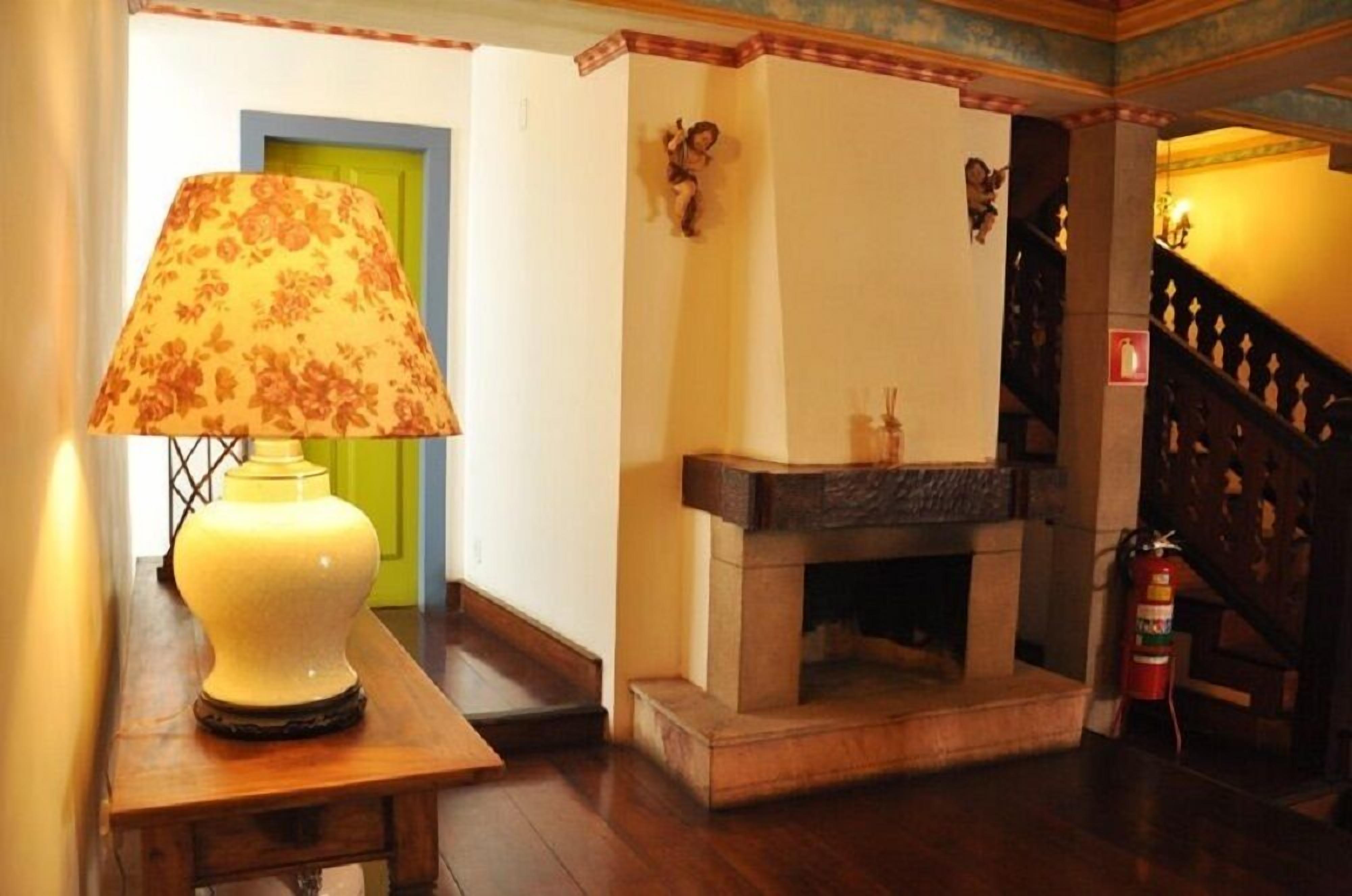 A room with a wooden table, a lamp, a green door, a fireplace, and a staircase.