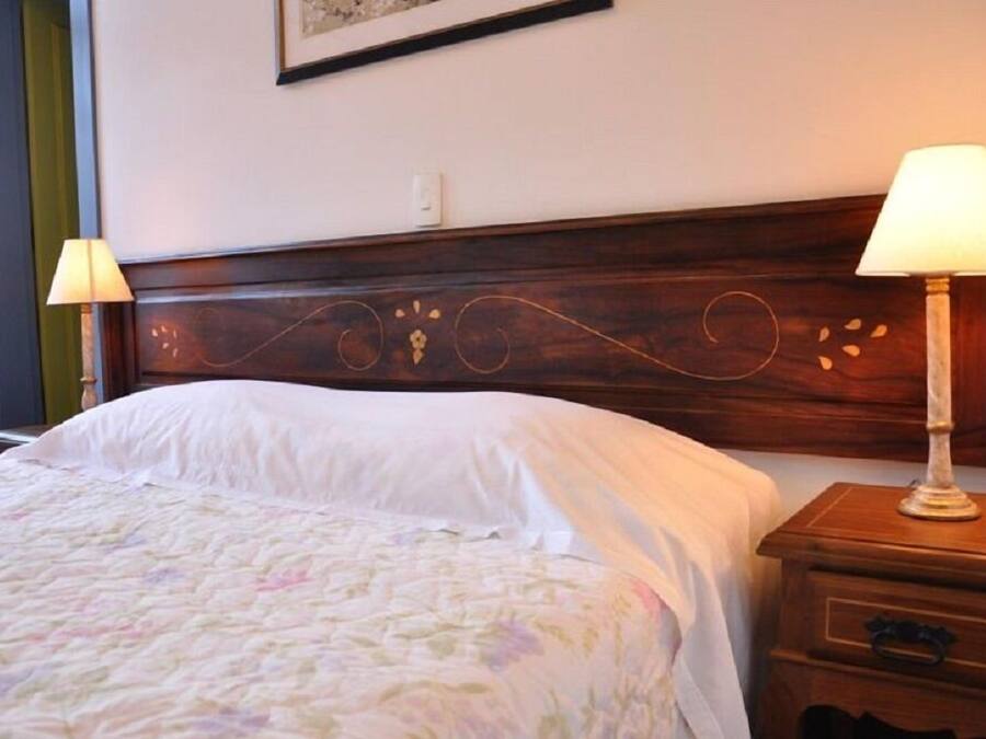 A neatly made bed with a floral bedspread, a wooden headboard with decorative carvings, and two bedside lamps on wooden nightstands.