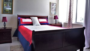 Un dormitorio ordenado con una cama grande, dos mesitas de noche, una lámpara y una ventana con cortinas, además de cuadros en la pared.