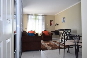 A living room with two sofas, a dining table with chairs, and a patterned rug.