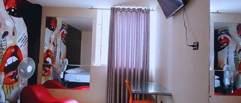 A hotel room with two beds, a desk, a chair, a TV mounted on the wall, and a window with curtains.
