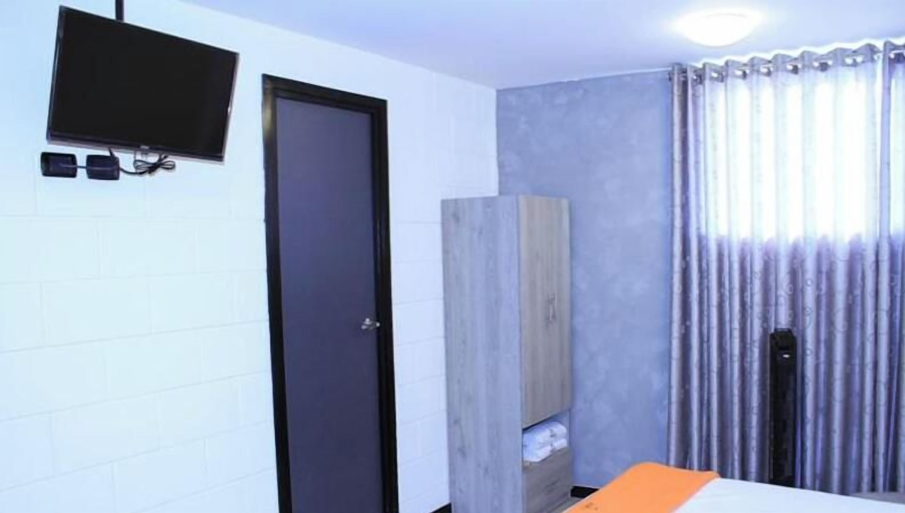 Una habitación con cama, una puerta, un televisor montado en la pared y una ventana con cortinas.