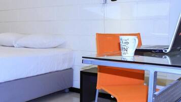 Habitación de hotel con una cama, una mesita de vidrio con una computadora portátil, una silla naranja y un aire acondicionado instalado en la pared.