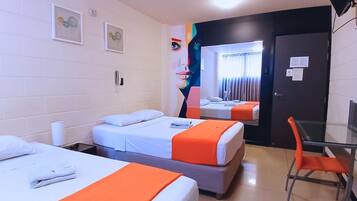 A hotel room with two beds, a desk, and a chair. There are pictures on the wall and a door with a mirror.