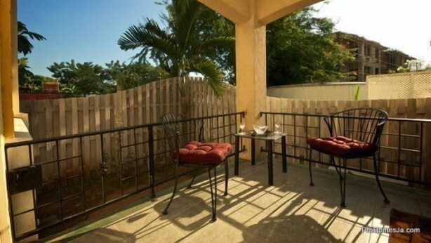 A balcony with a metal railing, two cushioned chairs, a small table, and a view of a cityscape with buildings and trees. - Winchester 12A by Pro Homes Jamaica (Kingston)