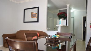 A living room with a brown sofa, a glass coffee table with a basket, a framed picture on the wall, and a potted plant on a shelf. - Winchester 12A by Pro Homes Jamaica (Kingston)