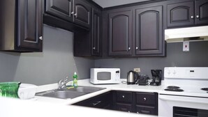 A kitchen with dark cabinets, a white stove, a microwave, a coffee maker, and a sink with dish soap. - Winchester 12A by Pro Homes Jamaica (Kingston)