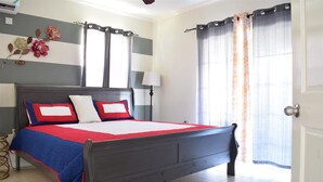 A bedroom with a bed, a nightstand, a lamp, and a window with curtains. - Winchester 11A by Pro Homes Jamaica (Kingston)