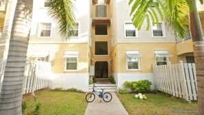 A two-story residential building with a central entrance, a bicycle parked in the front, and a white picket fence. - Winchester 11A by Pro Homes Jamaica (Kingston)