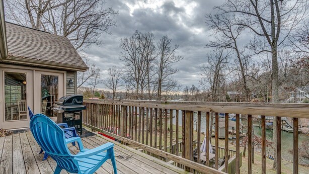 A wooden deck with a blue chair and a grill, overlooking a body of water and trees. - Winchester 11A by Pro Homes Jamaica (Kingston)
