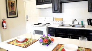 A kitchen with white cabinets, a stove, a sink, and a dining area with a table set for two. - Winchester 11A by Pro Homes Jamaica (Kingston)