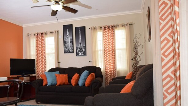 A living room with a black sofa, orange and blue cushions, a television, and two framed pictures of the Eiffel Tower. - Winchester 07A by Pro Homes Jamaica (Kingston)