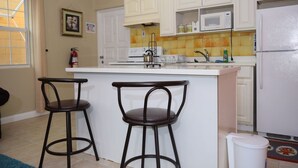 A kitchen with white cabinets, a white island with two stools, a microwave, and a refrigerator. - Winchester 07A by Pro Homes Jamaica (Kingston)