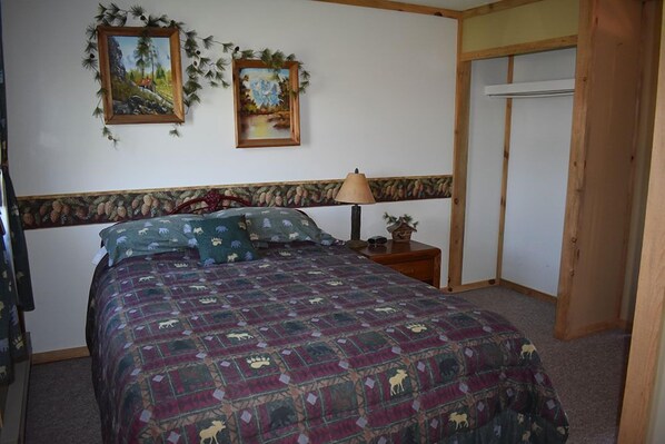 A bedroom with a bed, two paintings, a lamp, and a wooden wardrobe. - Beartooth Basin Bunkhouse (Belfry)