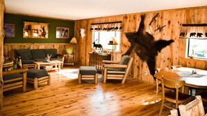 A rustic cabin interior with wooden walls, a dining table, and a sofa. - Beartooth Basin Bunkhouse (Belfry)