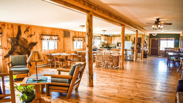 A spacious lodge with wooden floors, a dining area, and a kitchen. - Beartooth Basin Bunkhouse (Belfry)