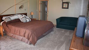 A bedroom with a large bed, a green sofa, a wooden dresser, and a television. - Beartooth Basin Bunkhouse (Belfry)