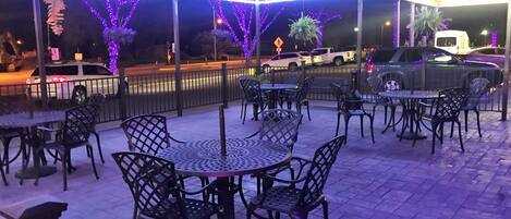 Eine Außenpatio-Terrasse mit Tischen und Stühlen, dekoriert mit violetten Lichtern.