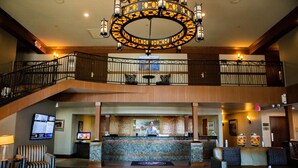 A hotel lobby with a reception desk, a staircase, and a chandelier.